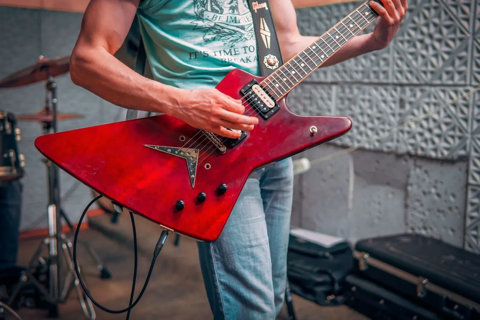 Musician playing electric guitar with a drum kit set up behind, the kind of backline a rehearsal room provides