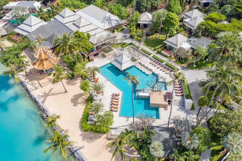 Vue aérienne de la piscine, de la plage de sable et du toit de pagode orange de Fair House Villas & Spa parmi les cocotiers