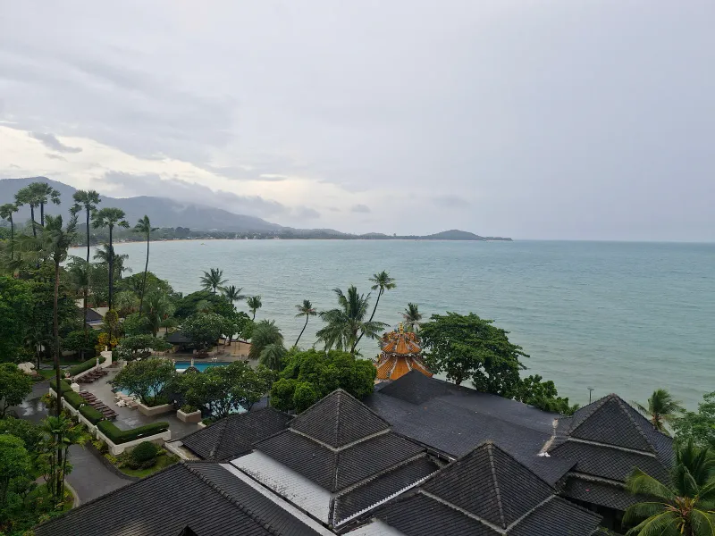Vue par-dessus les toits et la piscine de Fair House Villas & Spa vers la longue courbe de la baie de Maenam