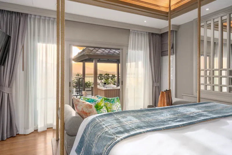 Chambre de suite avec lit à baldaquin suspendu à des cordes et jacuzzi sur la terrasse donnant sur la baie au coucher du soleil