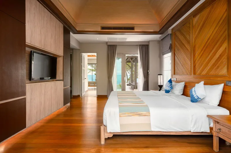 Chambre de villa lambrissée de teck à Fair House Villas & Spa, avec grand lit blanc et vue sur la mer par la porte
