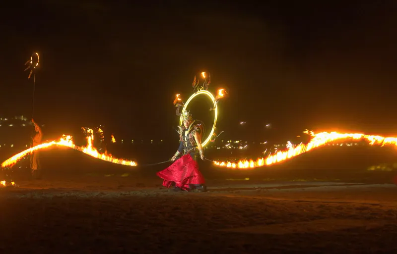 A fire dancer performing with trails of fire at a night beach show