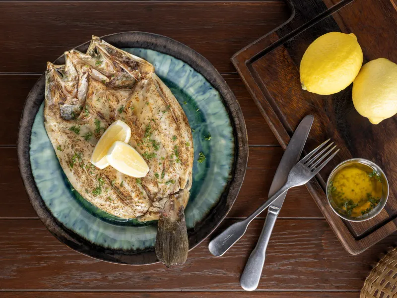 Whole grilled fish with lemon wedges and herb butter, a signature seafood dish at FishHouse Restaurant, Kimpton Kitalay Samui, Koh Samui