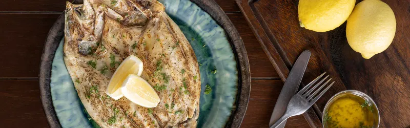Close-up of a whole grilled fish with lemon wedges, a seafood specialty at FishHouse Restaurant, Kimpton Kitalay Samui