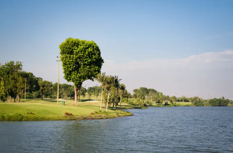 A green golf course beside a lake under a bright blue sky in Thailand