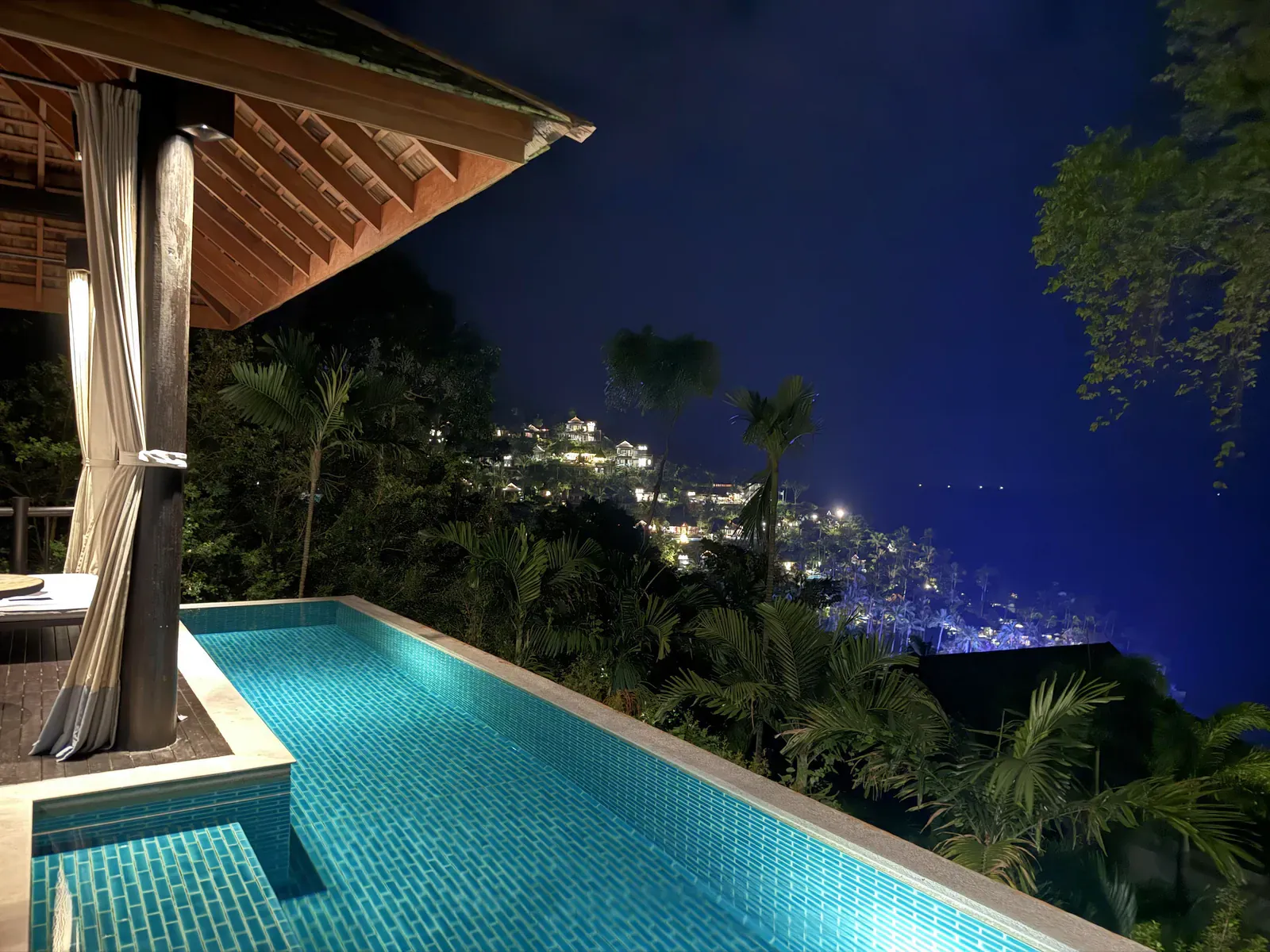 Eine Poolvilla des Four Seasons Koh Samui bei Nacht, darunter die Lichter der Bucht