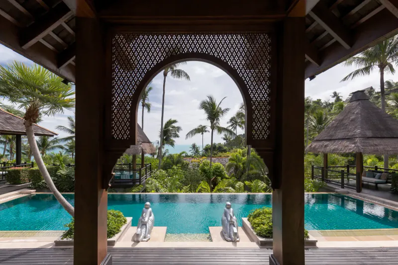 Pavillon à arche sculptée encadrant une piscine à débordement de villa et la colline au Four Seasons Resort Koh Samui