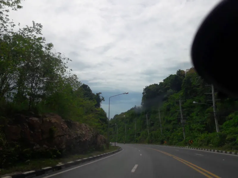 Hillside jungle road with red laterite rock cutting near Koh Samui's northwest coast, close to Laem Yai Bay