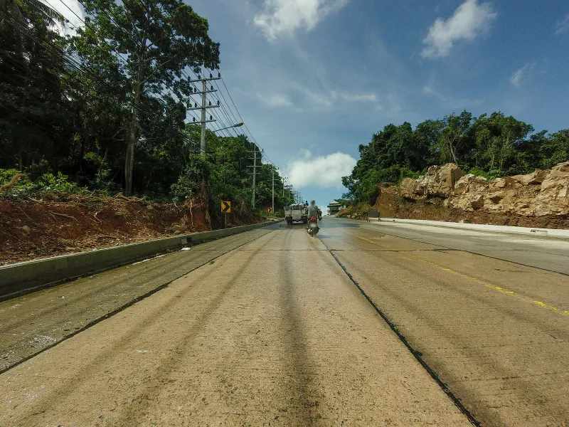 Two-lane hillside road with rocky embankment on the approach to Four Seasons Resort Koh Samui