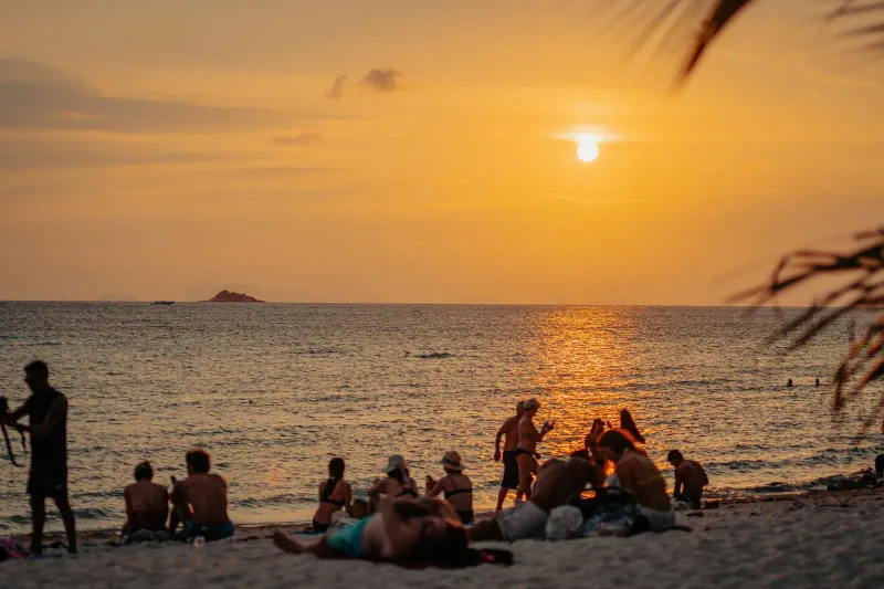 Tourists relaxing on the beach at sunset ahead of a night boat trip from Koh Samui to Haad Rin