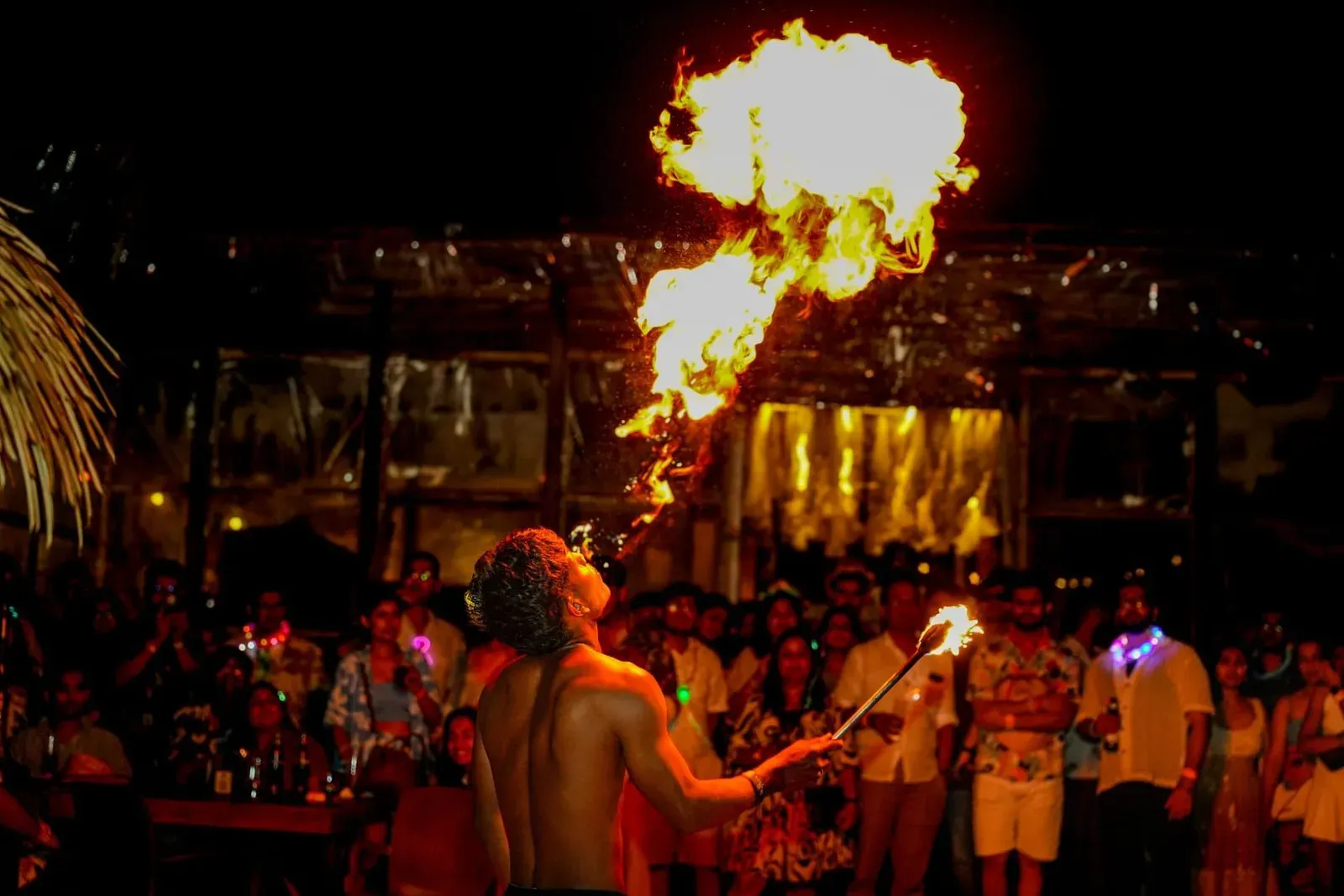 Fire performer entertaining a large crowd at an outdoor night party, similar to the beach stages that line Haad Rin during the Full Moon Party