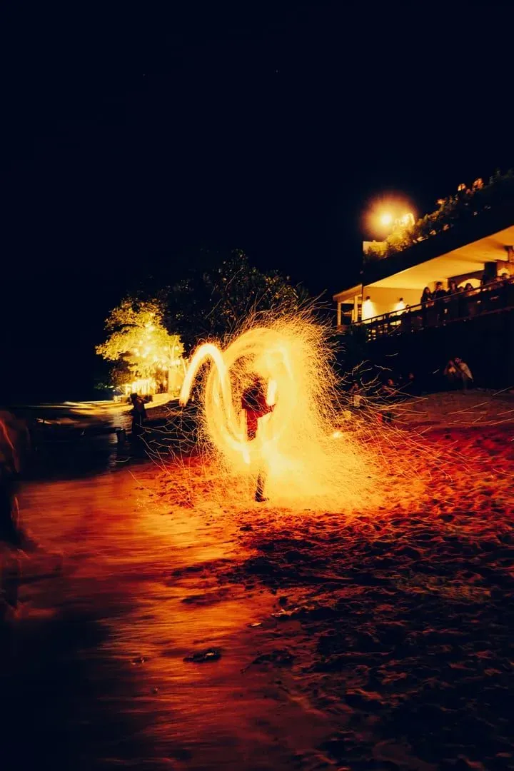 Fire dancer performing on a tropical beach at night in front of a watching crowd, the kind of act found nightly along Haad Rin's Full Moon Party strip