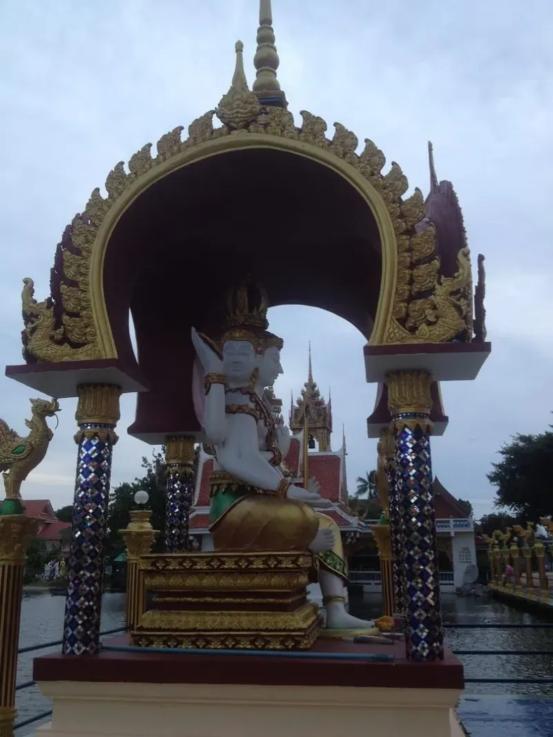 Eine vielarmige Gottheitsstatue unter einem prunkvollen Torbogen im nahegelegenen Wat Plai Laem