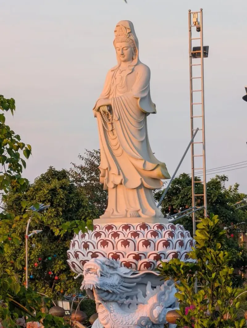 Eine friedliche weiße Guanyin-Statue steht im Freien auf einem Drachensockel inmitten üppigen Grüns