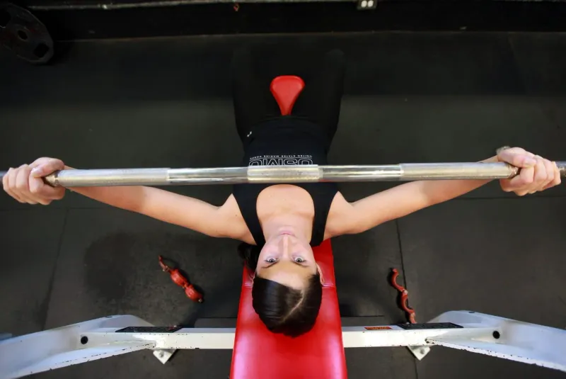 Woman lying on a bench press bench gripping a loaded barbell overhead, viewed from directly above