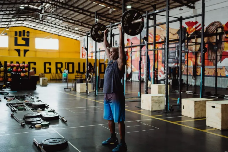 Man performing an overhead barbell lift in an industrial-style gym, the strength training style at BXB Fight Lab Lamai