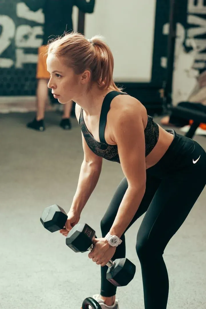 Woman performing a bent-over dumbbell row in a gym with black rubber flooring
