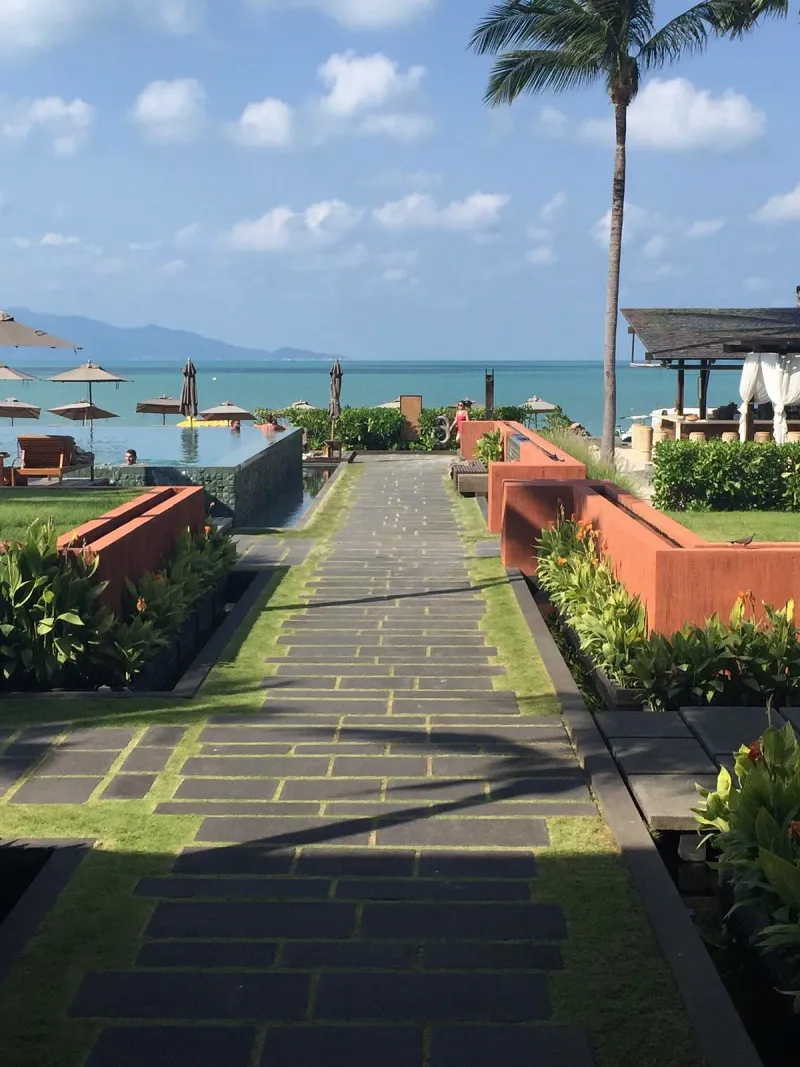 Sentiero di pietra tra muri di terracotta curati che porta alla piscina e al mare dell'Hansar Samui