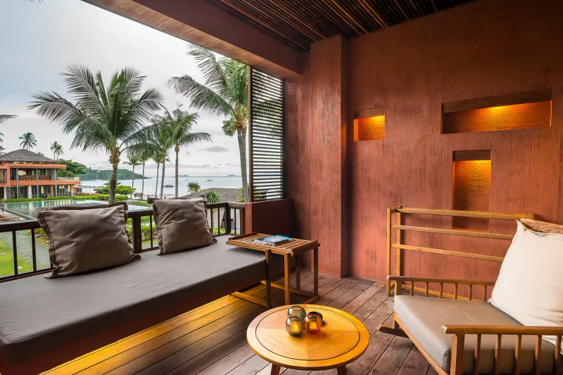 Letto da giorno sul balcone dell'Hansar Samui con cuscini, schermi di legno e palme sopra la baia