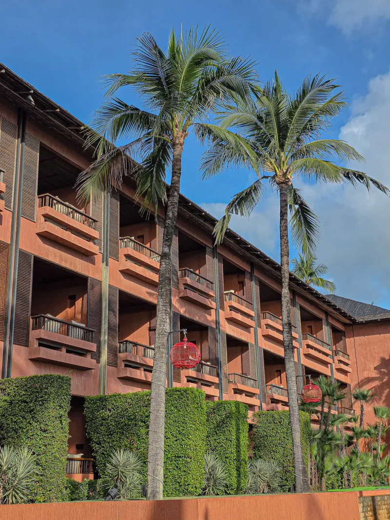 Blocco di camere in terracotta dell'Hansar Samui con balconi a più livelli e alte palme da cocco contro il cielo azzurro