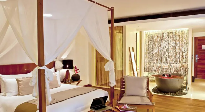 Camera con letto a baldacchino bianco, pavimento di legno e una vasca di pietra all'Hansar Samui