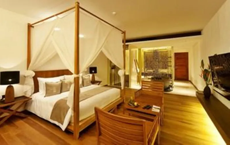 Camera dell'Hansar Samui con letto a baldacchino, poltrone e un pavimento di legno che porta al bagno