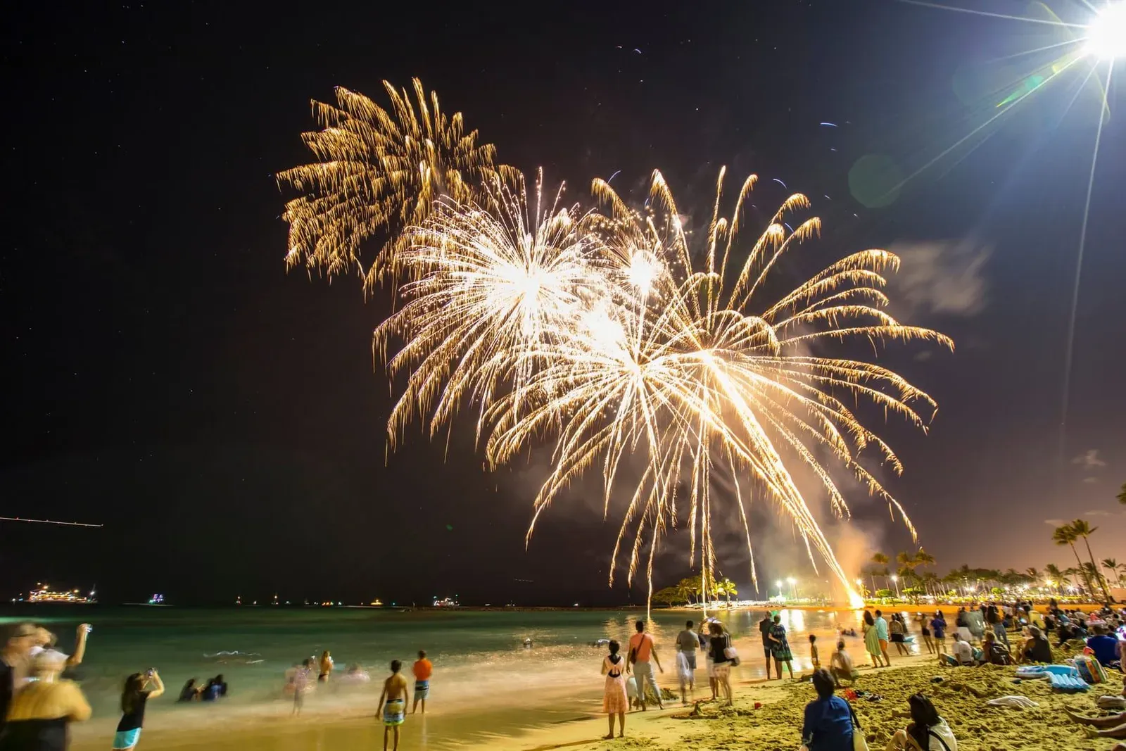 Colorful fireworks bursting above a packed beach crowd during a New Year's Eve countdown party