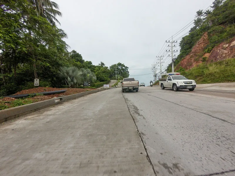 Concrete coastal road winding through jungle hillside near Laem Yai, the access route to Four Seasons Resort Koh Samui