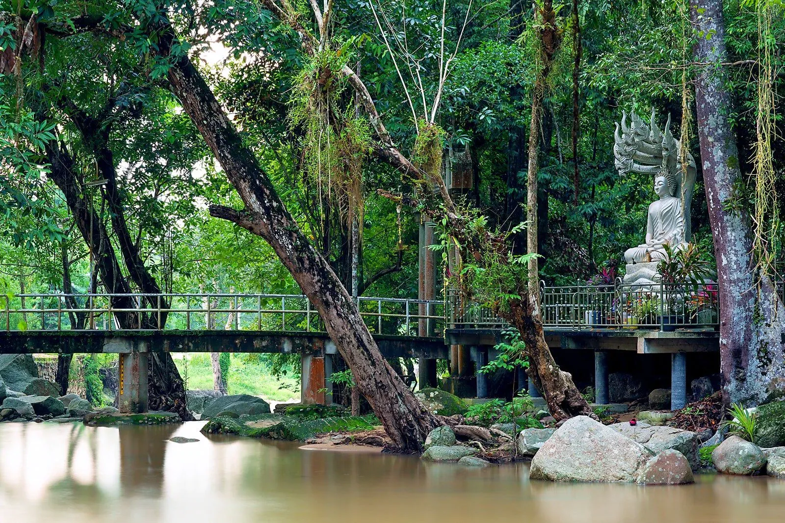 Buddha-Statue und Fußgängerbrücke über den Fluss bei Wat Namtok Hin Lat