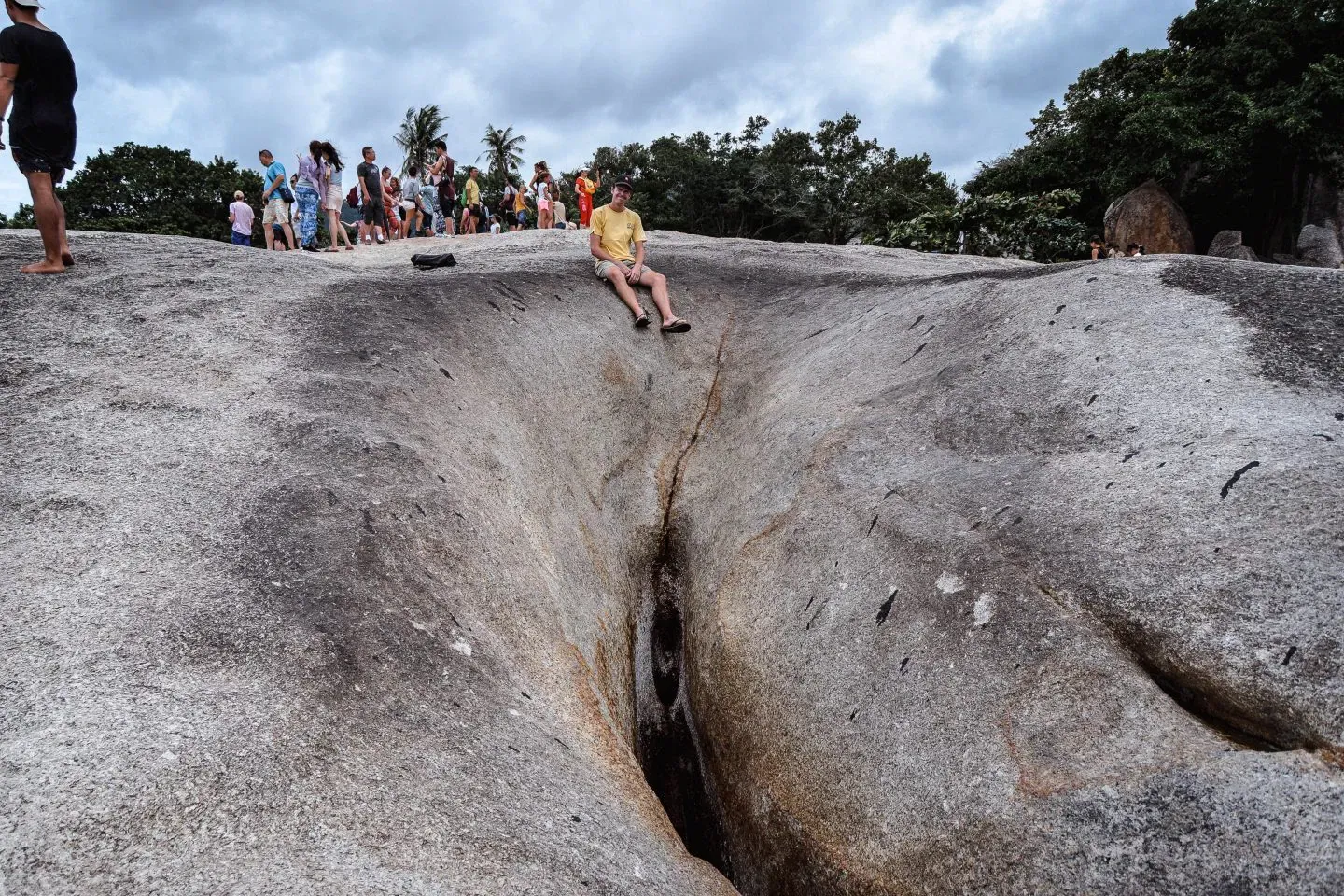 A visitor sitting in the narrow cleft of Hin Yai, the grandmother rock, with a crowd of onlookers behind