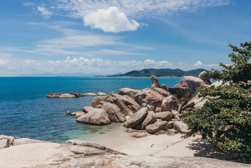 An elevated view of the Hin Ta Hin Yai boulder field, sandy cove and coastline stretching into the distance