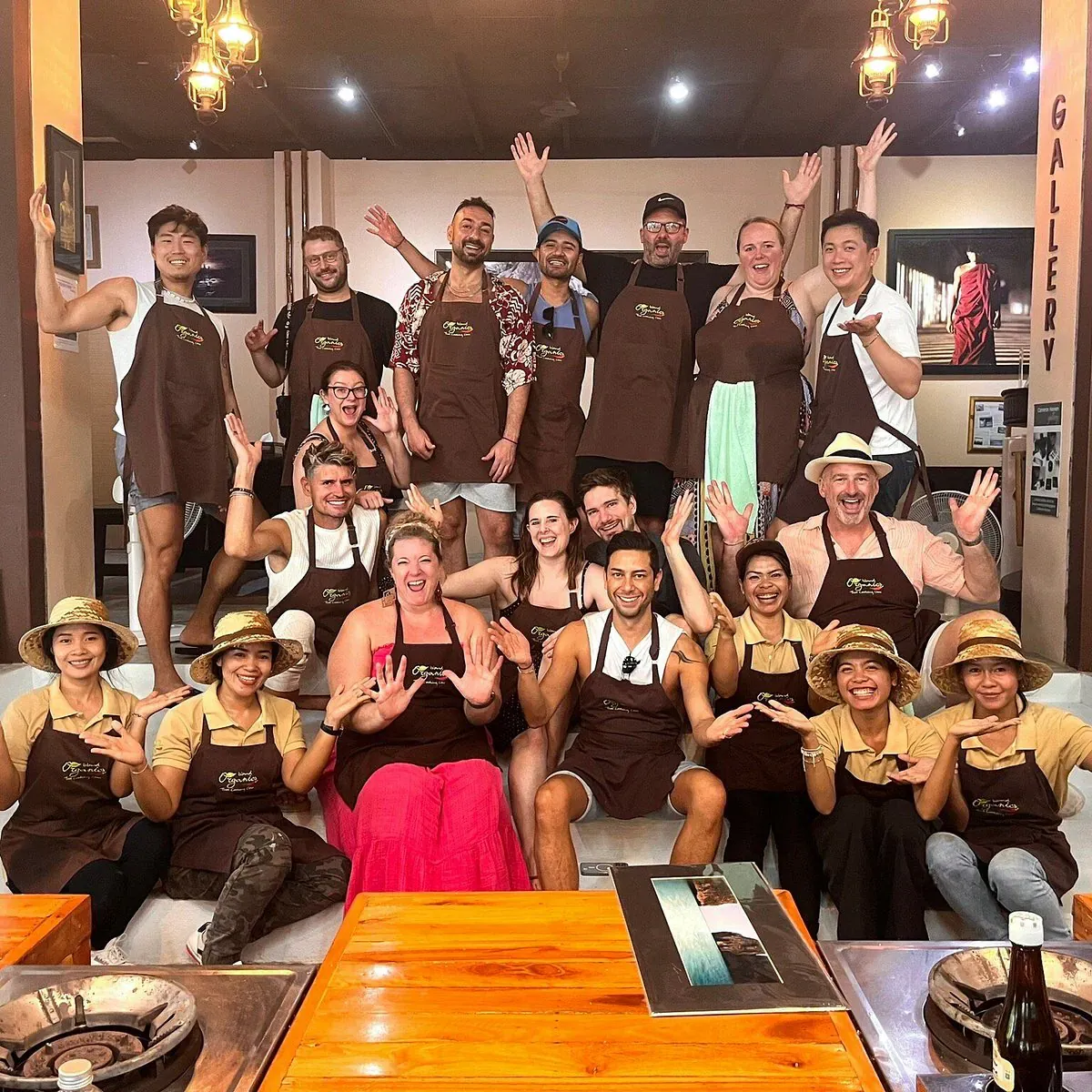 A group of Island Organics Samui cooking class guests posing in branded aprons after a class