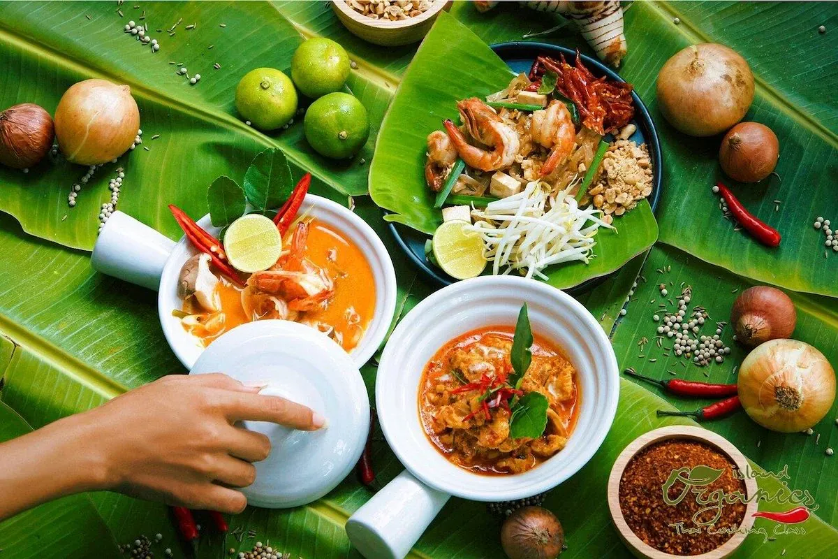 Thai curry and soup dishes plated on banana leaves with fresh chillies and limes, branded Island Organics Thai Cooking Class