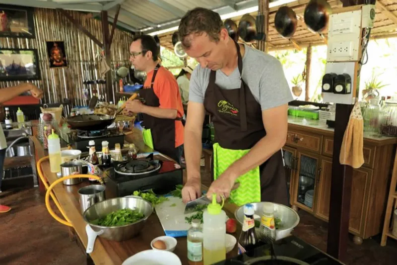 A guest chopping herbs at Island Organics Samui, wearing the school's branded apron