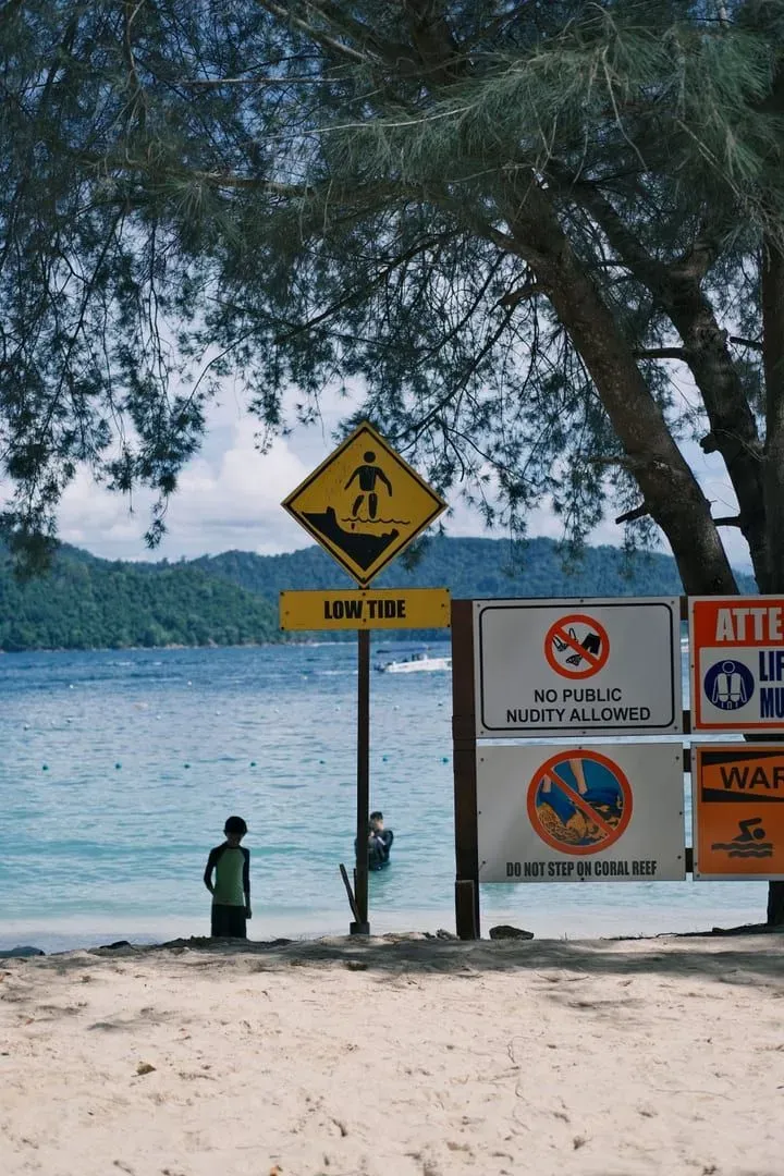 Tropical beach scene with posted warning signs and low tide conditions
