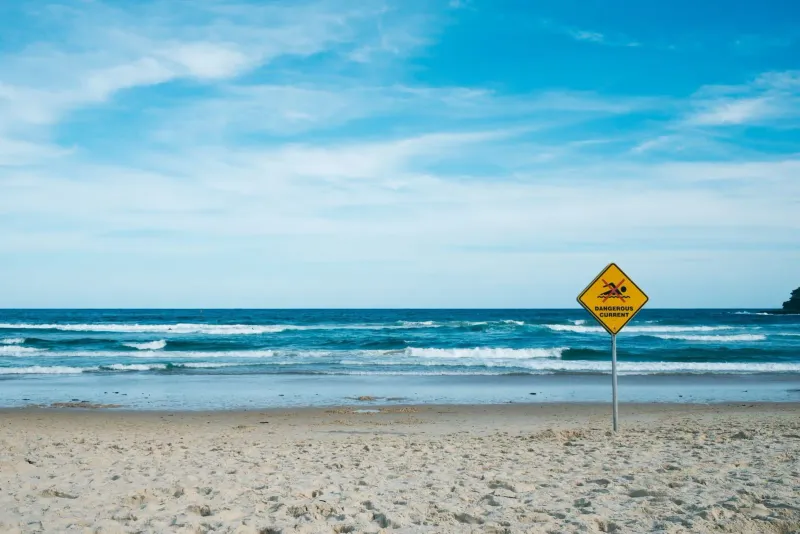 Warning sign about dangerous marine currents beside a calm blue sea