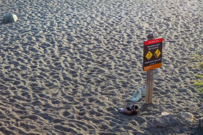 タイの砂浜の海岸に、靴が置かれたそばの警告看板