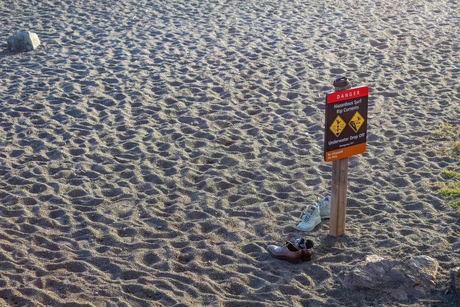 Beach warning sign with shoes left nearby on a sandy Thailand shoreline