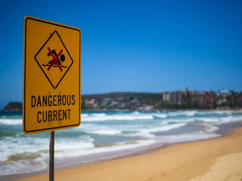 Yellow dangerous current warning sign on sand near ocean waves