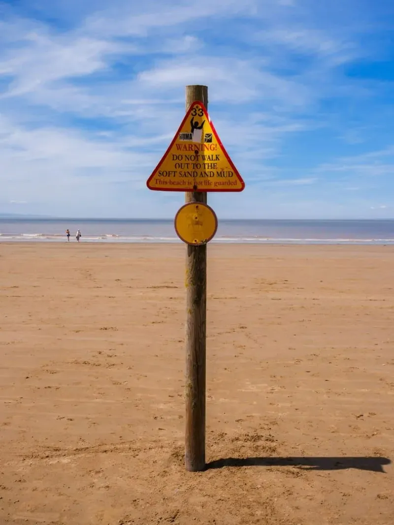 Beach hazard warning sign advising caution on soft sand and mud
