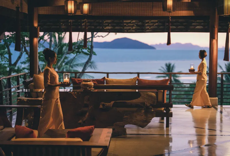 Personale che porta lanterne attraverso la terrazza all'aperto del ristorante del Kamalaya Koh Samui al tramonto