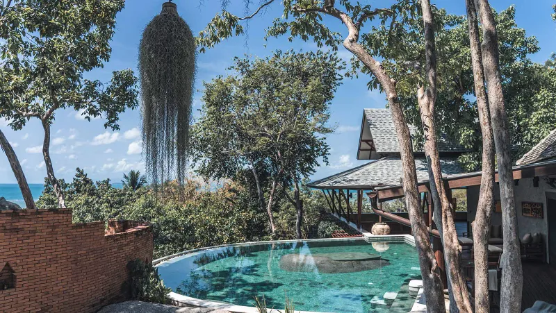 Piscina a sfioro incorniciata dagli alberi al Kamalaya Koh Samui con un padiglione di paglia più in là