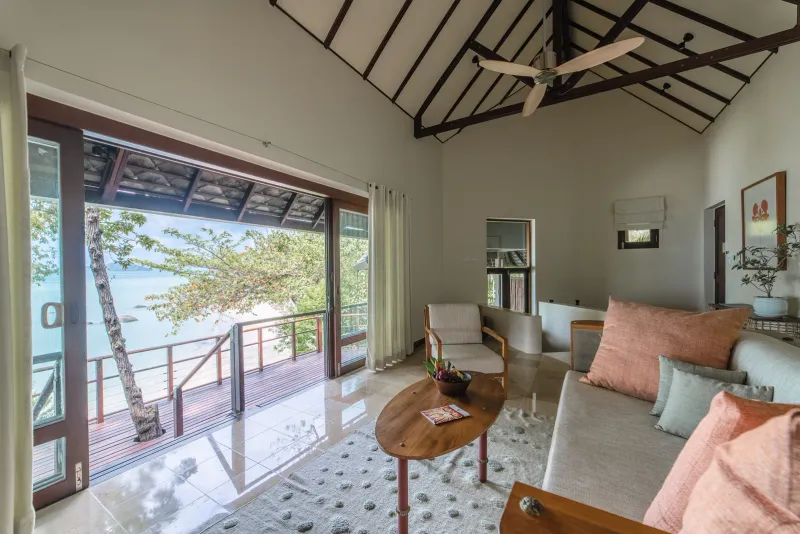 Salotto di una suite del Kamalaya Koh Samui con vista mare attraverso le porte aperte e una terrazza di legno