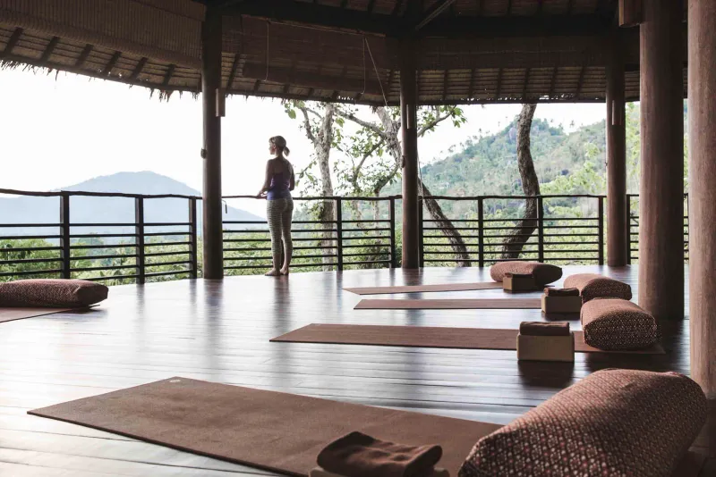 Padiglione yoga con i lati aperti, tappetini e cuscini lunghi, affacciato sulle colline boscose del Kamalaya Koh Samui
