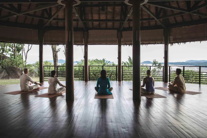 Gäste sitzen auf Matten für eine Gruppenmeditation in einem offenen Pavillon
