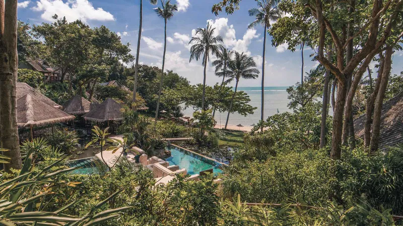 Luftaufnahme des gefliesten Pools des Resorts zwischen Gärten und strohgedeckten Dächern