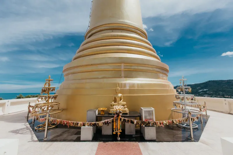 Base of the golden chedi with a small Buddha shrine and prayer ribbons on the terrace