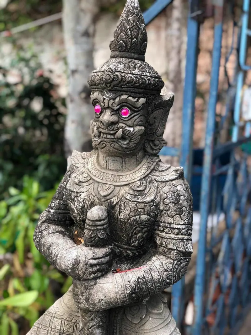 Weathered stone guardian giant statue with painted eyes at a Koh Samui temple