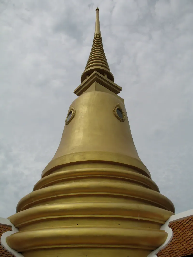 Close-up of the golden bell-shaped chedi spire against a cloudy sky