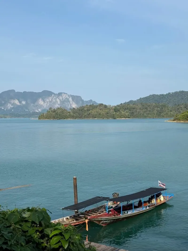 Longtail boat drifting on serene Cheow Lan Lake surrounded by jungle-covered karsts